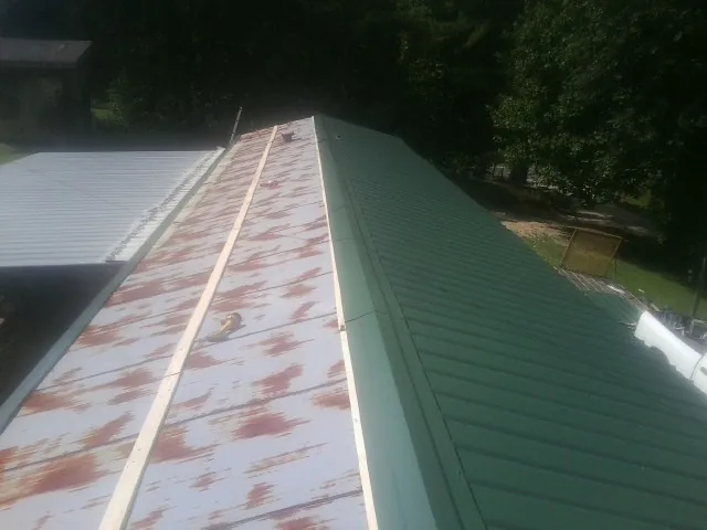 Old rusted panels beside newly installed green metal roofing — Wind Damage Roof Repair by Roofing Brothers in Ava