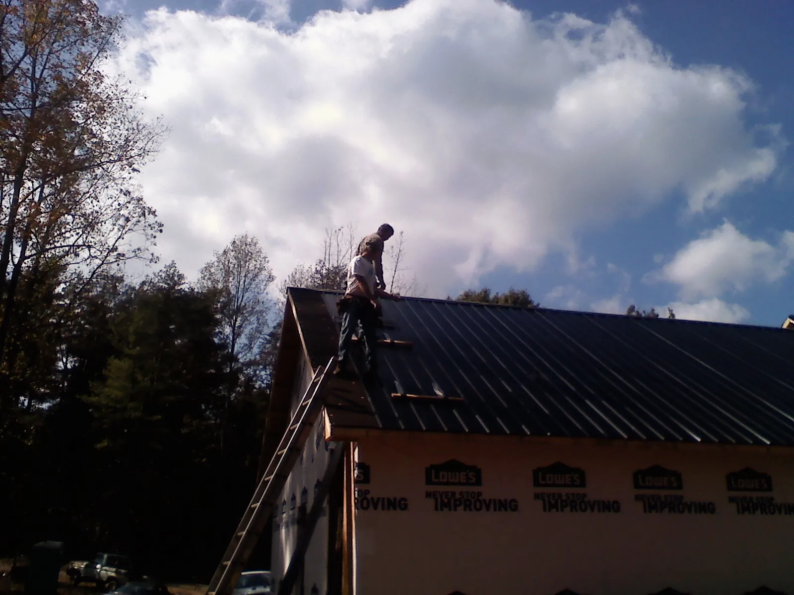 Roofer fastening dark metal panels high against a cloudy sky, from a Roof Inspection job in Ava