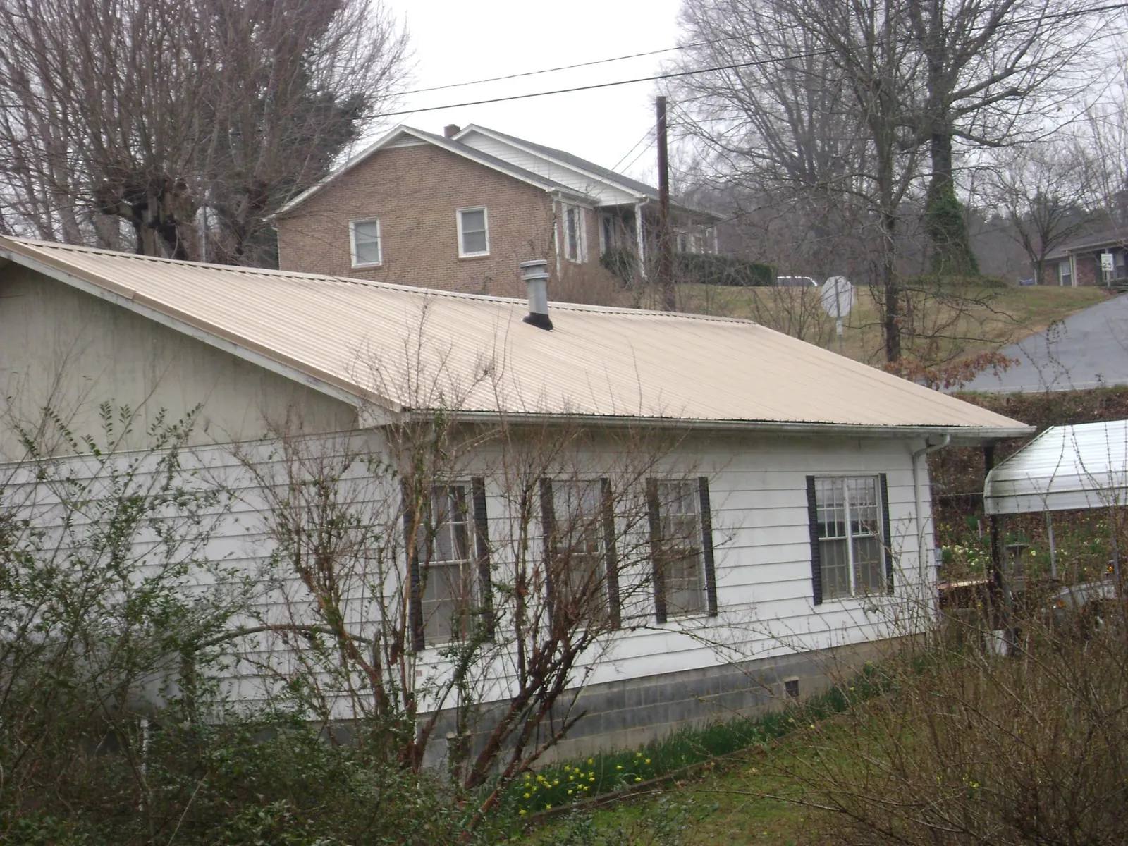 Tan metal roof on a white sided house set into a hillside — Commercial Roofing by Roofing Brothers in Ava