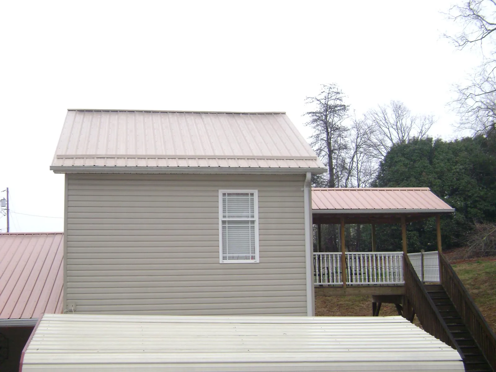 Tan metal roofs on a two story addition and attached porch, from a Roof Replacement job in Ava